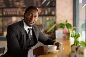Portrait of handsome bearded African businessman in suit relaxing at the coffee shop